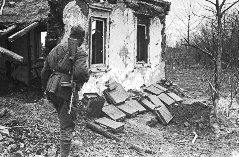 Un soldat de l'Armée rouge près d'une maison détruite et des boîtes d'obus pour le canon allemand Pak 35/36