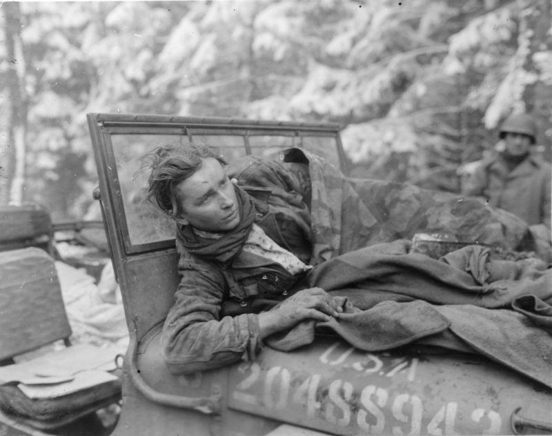 Un jeune soldat SS capturé blessé se trouve sur le capot d'une jeep américaine dans les Ardennes. 6 janvier 1945